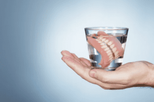 Dentures soaking in a clear glass of water. Singular hand is holding the glass of water dentures restorative dentistry dentist in Nashville Tennessee